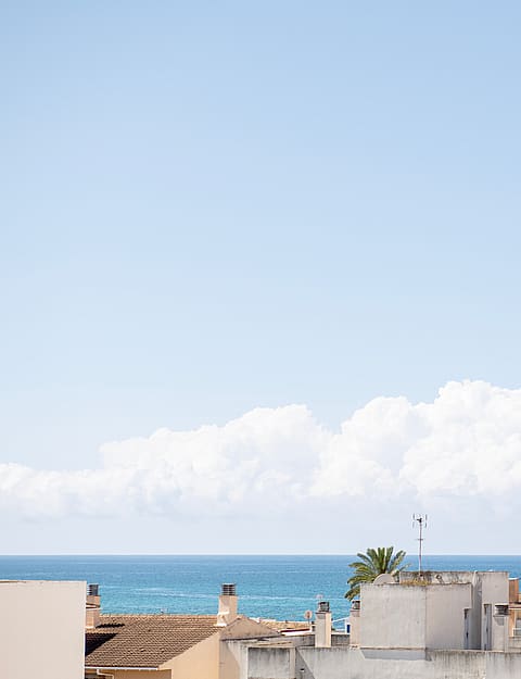 An elevated view looking out over the flat rooftops of El Molinar towards the blue Mediterranean Sea under a clear sky.