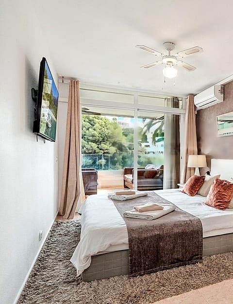 A modern bedroom featuring a large bed with neutral linens, a textured terracotta feature wall, and glass sliding doors leading to a private terrace.