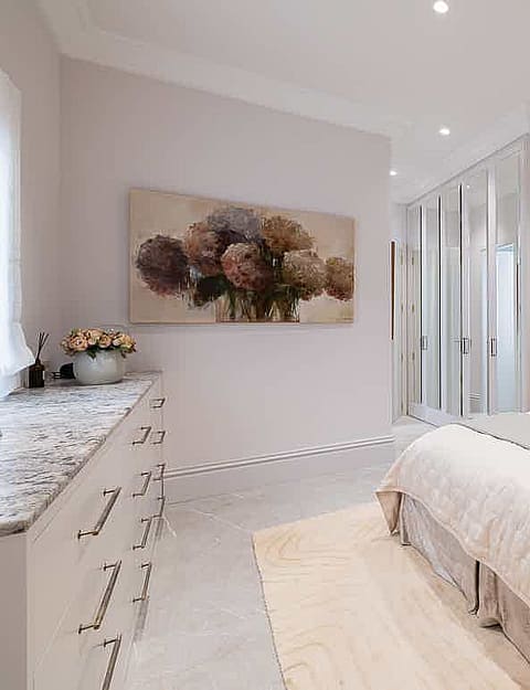 Bedroom featuring a large tufted velvet headboard, white wardrobe doors, and a floral painting on a light grey wall.