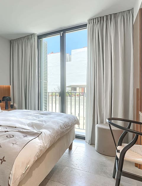 Bright bedroom with a double bed, vertical oak wood wall paneling, and floor-to-ceiling glass doors with light curtains.