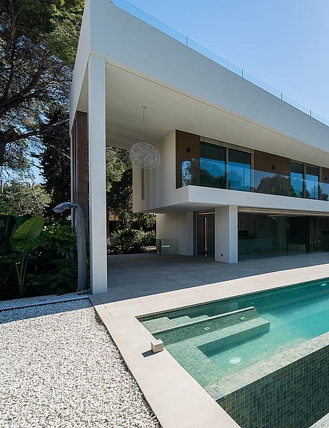 Contemporary white villa in Santa Ponsa with a long rectangular swimming pool, stone accent wall, and landscaped garden.