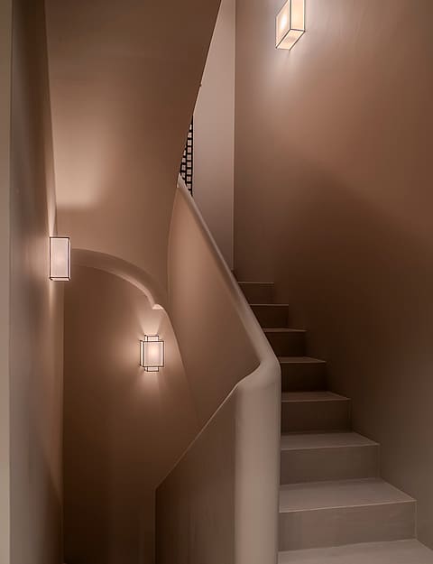 A minimalist internal staircase featuring curved plaster handrails and integrated warm wall sconces in soft sand tones.