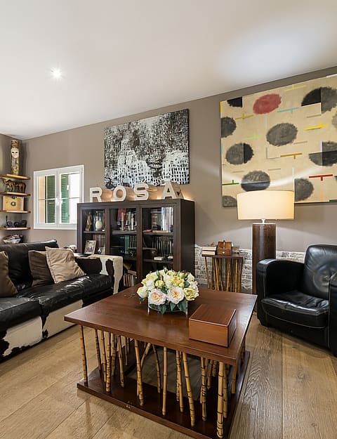 Interior view of a living room with dark leather sofas, a wooden coffee table, large abstract art, and a recessed fireplace.