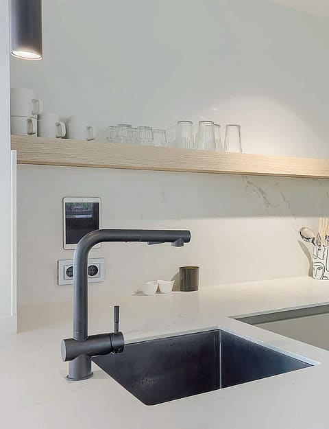 Modern kitchen featuring matte white cabinets, light wood shelving, and a dark faucet above a stainless steel sink.