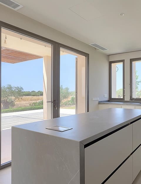 Modern kitchen with large central island, white cabinetry, integrated appliances, and view through glass doors to patio.