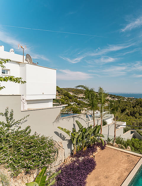 High angle shot of a minimalist white villa exterior with a swimming pool and landscaped garden overlooking the Mediterranean coastline.