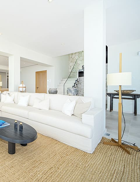 Bright open-plan living room in Illetas with white sectional sofa, oval coffee table, and a large textured jute rug.