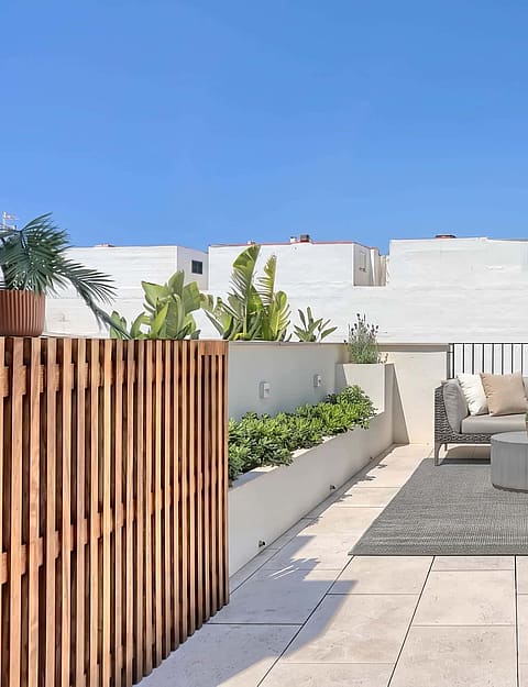 A spacious rooftop terrace featuring a modular outdoor sofa set on a textured rug, bordered by a wooden screen and stone walls.