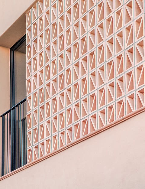 Close-up of a pink plastered townhouse exterior featuring a geometric terracotta breeze block screen and black metal railing.