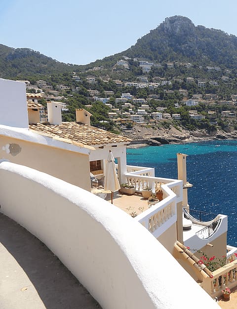 High angle shot of a multi-level stone terrace overlooking a turquoise Mediterranean bay with sun reflecting off the water.