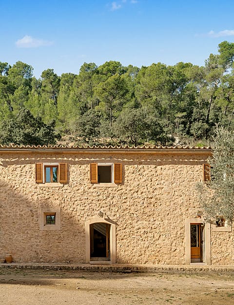 Two-storey stone finca façade with wooden shutters and dry-stone walls
