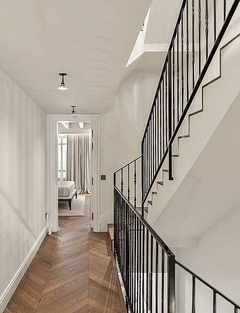 Interior hallway featuring herringbone wood floors, black metal staircase railings, and a view into a bedroom.