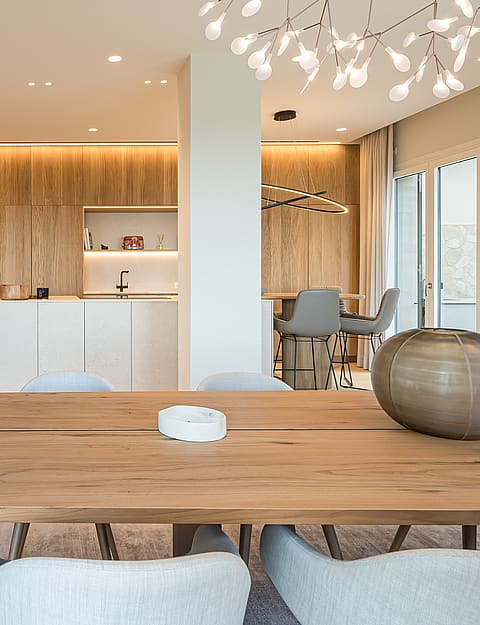 Dining room featuring a long wooden table, light grey upholstered chairs, and a floor-to-ceiling built-in wine fridge in a black frame.