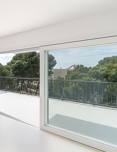 Modern white kitchen featuring a matte island with an oak breakfast bar and sliding glass doors opening to a balcony.