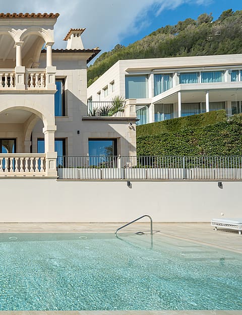 Two-story Mediterranean villa featuring stone arches and balustrade balconies overlooking a rectangular swimming pool.