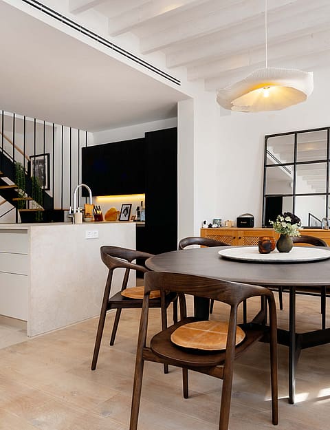 Dining room with a round wooden table, black chairs, and a metal staircase leading to the upper floor.