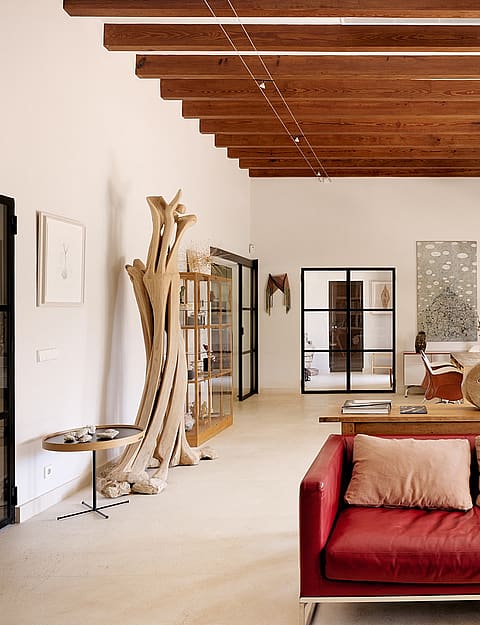 A spacious living room with high beamed ceilings, red leather sofa, and white walls in a Finca-style home.