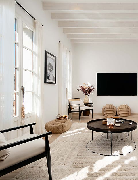 Living room with black cane armchairs, a cream linen sofa, black round coffee tables and framed black and white photography.