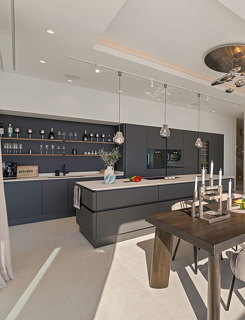 Modern open-concept interior featuring a dark grey kitchen island, a wooden dining table with light chairs, and recessed ceiling lighting.