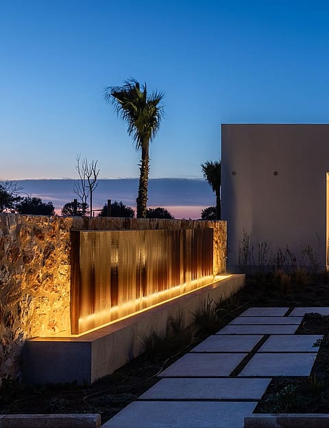 Contemporary stone and render finca exterior at dusk with linear landscape lighting, stone pathways, and glowing interior.