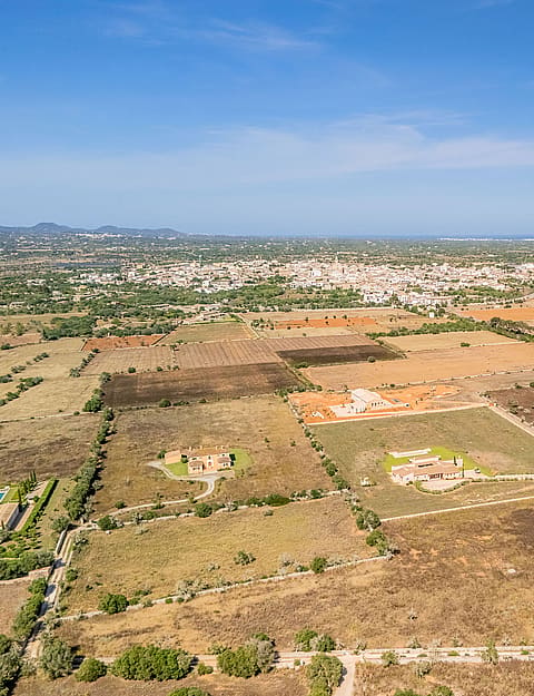 High-altitude aerial view of rural Mallorcan landscape near Santanyí, featuring sparse vegetation and distant town buildings.
