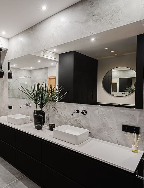 Modern bathroom featuring gray marble walls, a black floating vanity with double sinks, and a glass-enclosed walk-in shower.
