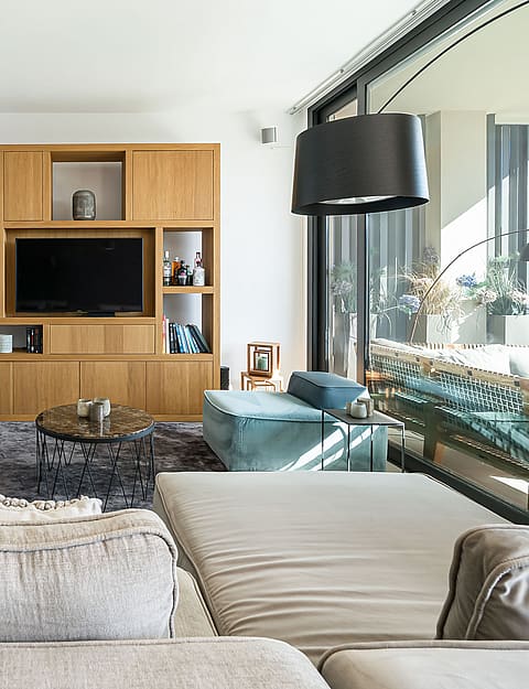 Modern living room with a large modular sofa, oak wood media wall unit, and glass sliding doors overlooking a terrace.
