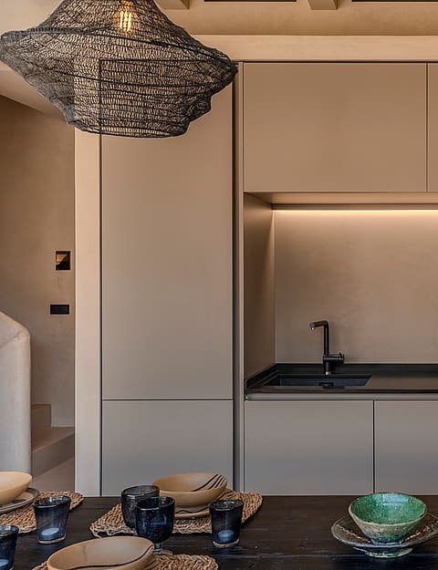 A minimalist kitchen wall featuring matte beige cabinetry, a dark countertop, integrated oven, and a sculptural textured pendant light.