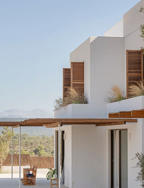 White contemporary villa featuring wooden slatted shutters and a timber pergola overlooking a mountain landscape.