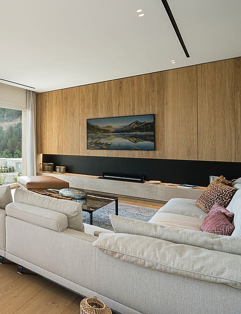 Spacious living room with beige sofa, wooden flooring, and floor-to-ceiling glass doors opening to a stone-railed terrace.