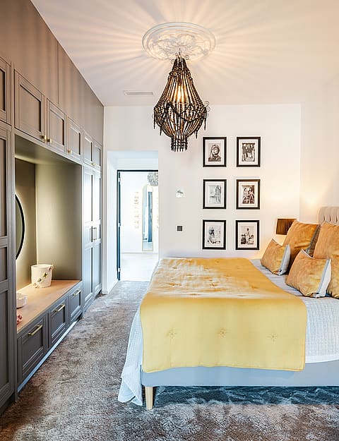 A modern bedroom featuring a large grey custom wardrobe unit, a tufted headboard, and mustard yellow bedding.