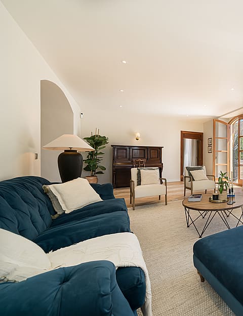 Living area featuring blue velvet tufted sofas, light herringbone wood floors, a dark piano, and arched patio doors.