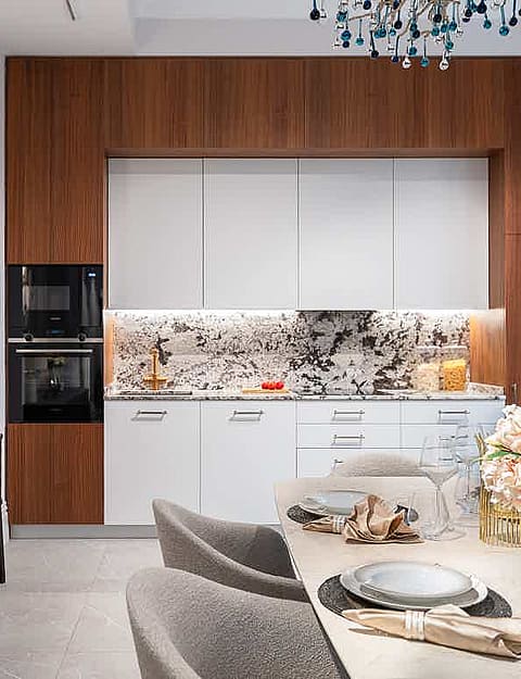 Modern kitchen with white cabinets, dark wood trim, and a patterned marble backsplash. Includes a side console and dining table.