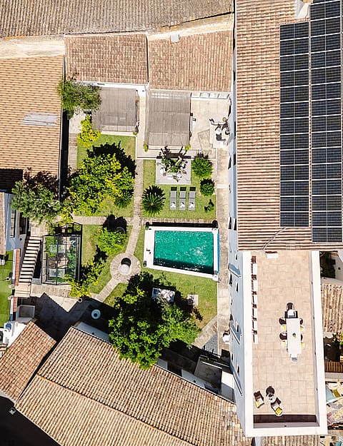 Overhead drone shot of a traditional townhouse in Sencelles, showing terracotta roof tiles, solar panels, a central garden, and a rectangular swimming pool.