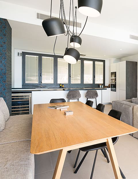 Modern open-plan living room with a beige sectional sofa, light oak wall unit, and a view into a white kitchen.
