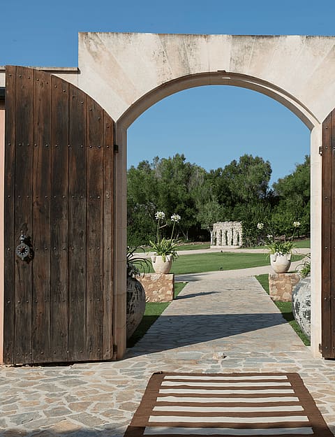 Wide-angle view of an open double-leaf wooden gate leading to a stone-paved courtyard with large terracotta pots.