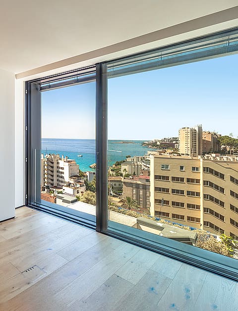 Modern bedroom interior featuring full-height oak wood cabinetry and floor-to-ceiling glass wall overlooking the sea.