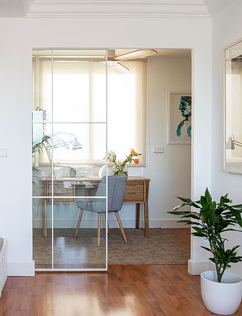 A white built-in bookshelf with a bench seat next to a glass-partitioned office area in a bright penthouse interior.