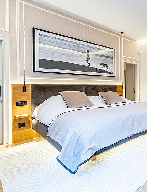 Spacious bedroom with a king bed on a light wood floor, soft cream walls, modern pop art, and an integrated white armchair.