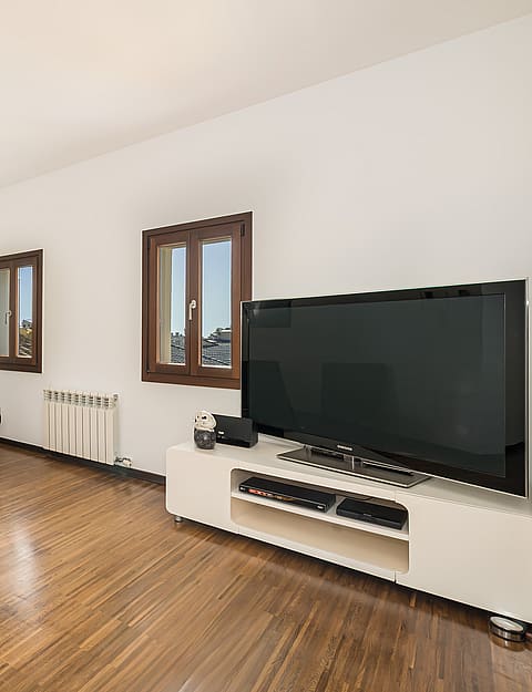 Living area with dark wood floors, navy leather chairs, white media console and wooden frame windows.