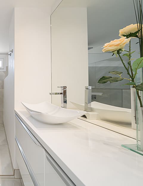 Interior of a modern bathroom with large light-toned floor tiles, a wall-hung toilet, a bathtub, and a sleek vanity sink.