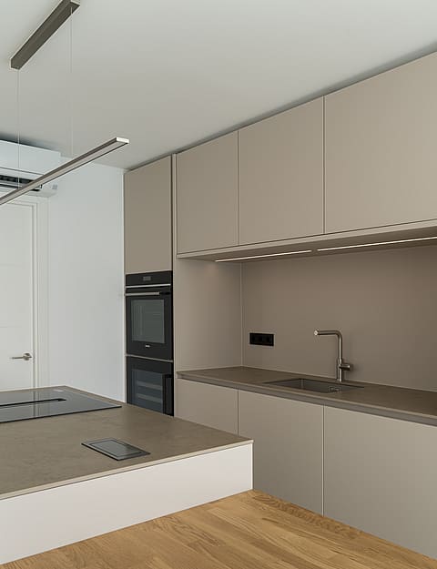 Modern kitchen featuring taupe cabinetry, oak flooring, stone worktops, and integrated double ovens.