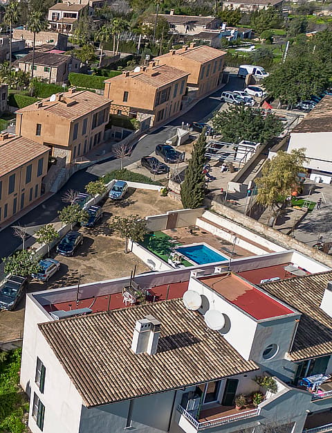 Aerial drone shot showing a row of stone-clad townhouses with terracotta tile roofs, private gardens, and small pools.