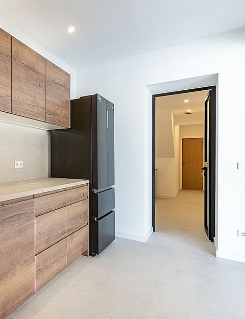 A modern kitchen in a townhouse features horizontal wood-grain cabinets, a matte black faucet, and a stone backsplash.