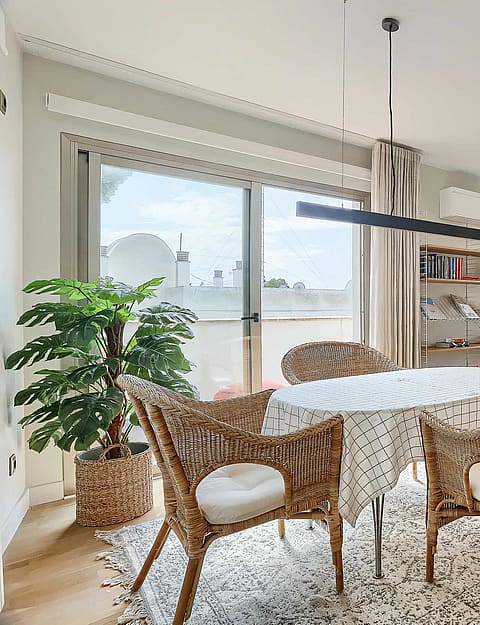 A bright dining area with a round table, wicker chairs, and large glass sliding doors opening onto a terrace with sea views.