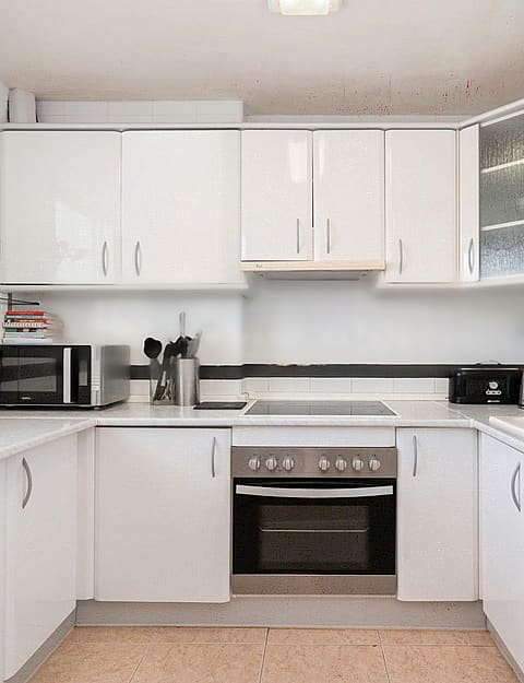 A bright galley kitchen with white cabinets, light countertops, and dark tiled backsplash, illuminated by natural light.