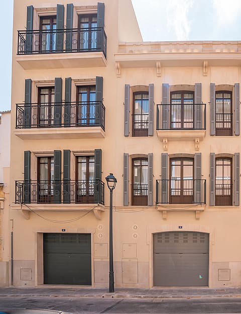A four-story cream stone townhouse featuring dark green shutters, Juliet balconies, and two ground-floor garage doors.