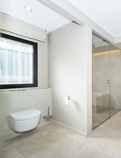 Modern bathroom featuring a beige stone-clad soaking tub, a glass-enclosed walk-in shower, and a wall-mounted toilet.