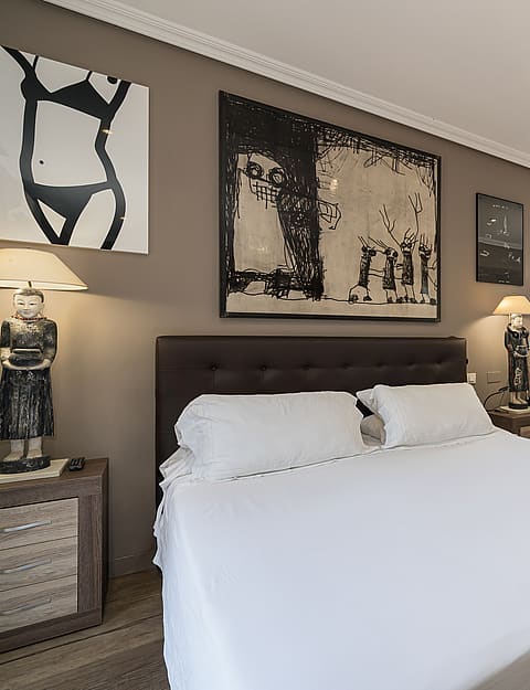 Bedroom with queen-sized bed, taupe walls, and an elevated bathroom area with a white soaking tub visible behind a low wall.