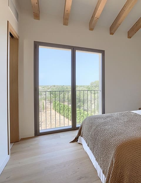 A bright bedroom featuring a queen bed with animal print bedding, light wood floors, and exposed ceiling beams with a balcony.